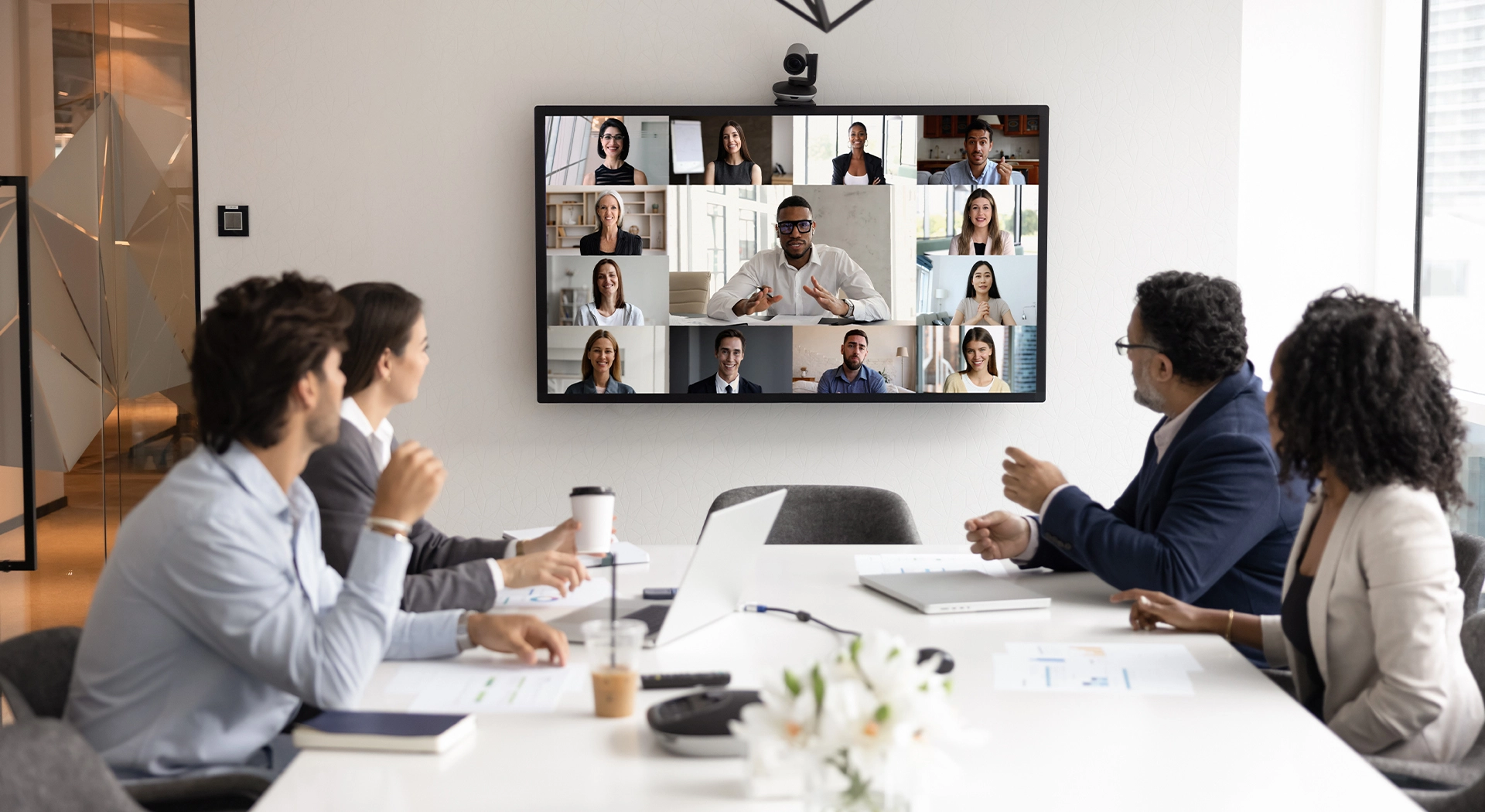 Cut-out image of Fabrick's head of Digital Content, Kate Aristides positioned next to a laptop showing numerous people's faces on a laptop screen